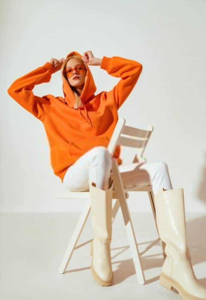 A girl dressed in an orange hoodie and white boots