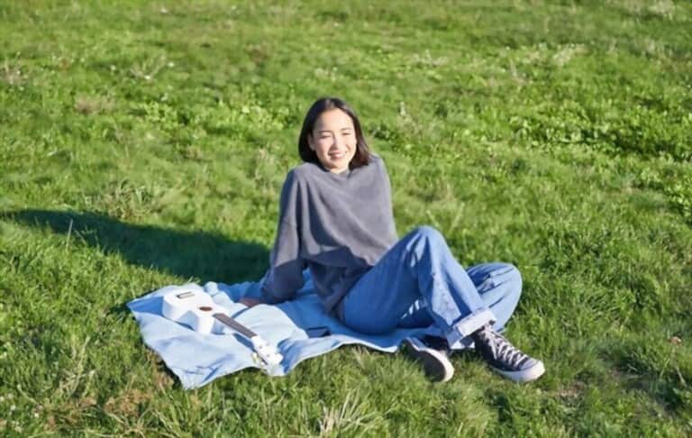 a young girl wearing blue jeans and warm sweater sitting on the grass