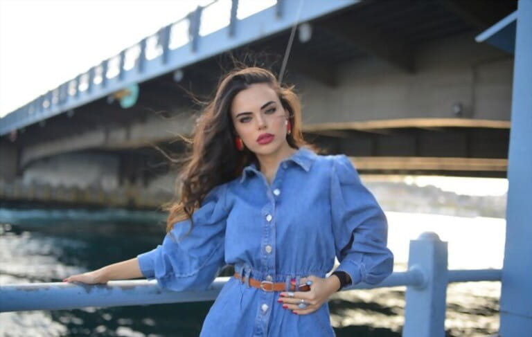 portrait of girl in blue jean dress with belt and transparent high heel on bridge in the street