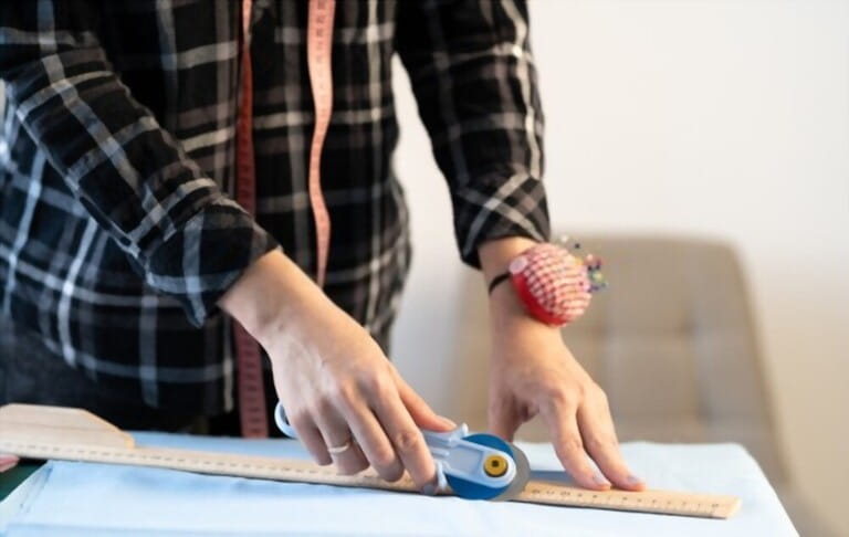 Close-up of a dressmakers hands cutting fabric along a sketch line using knife and ruler. Tailor working in a sewing workshop. Close-up of a dressmakers hands cutting fabric along a sketch line using knife and ruler. Tailor working in a sewing workshop.