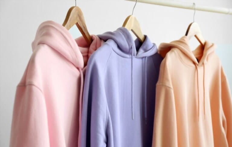 colorful hoodies (pink, purple and orange pastel) hanging on light wall