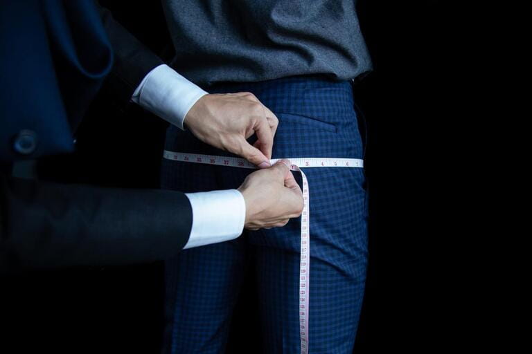 The dressmaker used a tape measure to measure the length of the hip on a black background. The dressmaker used a tape measure to measure the length of the hip on a black background.