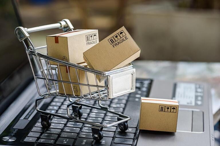 Multiple paper boxes in a small cart on laptop keyboard. The concept of online shopping where consumers can buy things directly from their home or office using just a few clicks through a web browser.
