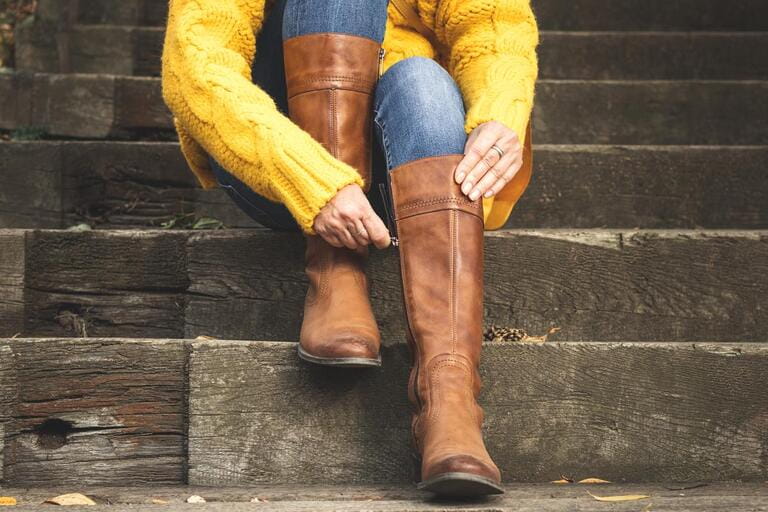 Woman sitting on stairs and fasten zipper on her leather boots. Autumn fashion concept