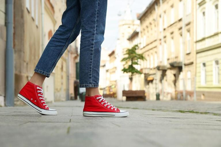 Woman in stylish sneakers walking on city street, closeup. Space for text