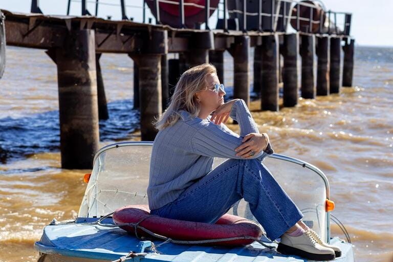 Portrait of a young beautiful girl in a blue sweater and jeans is on a boat near the river pier. Portrait of a young beautiful girl in a blue sweater and jeans is on a boat near the river pier.