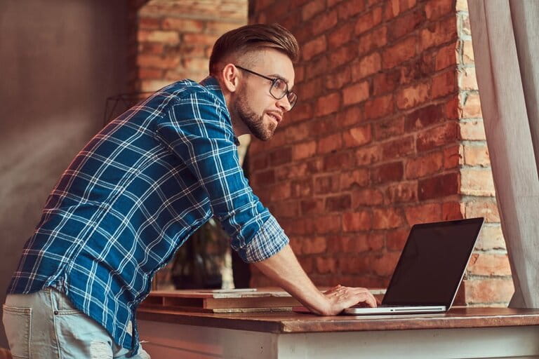 Handsome student in flannel shirt working on laptop in a room with loft interior. Handsome student in flannel shirt working on laptop in a room with loft interior.