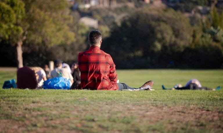 A man wearing a red flannel shirt sitting on grass at a park A man wearing a red flannel shirt sitting on grass at a park