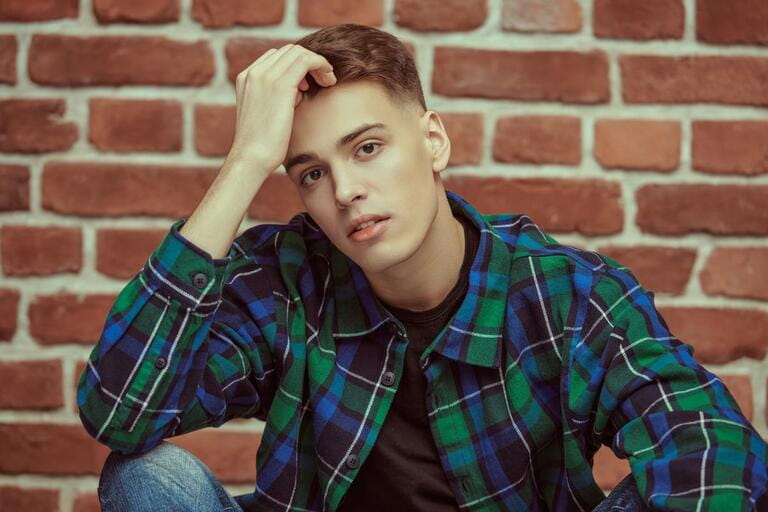 A handsome calm young man in a flannel plaid shirt against a brick wall. Youth fashion. People and emotions.