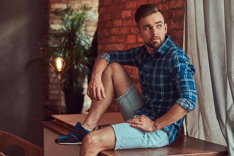 Handsome stylish bearded hipster sitting on a table in a room with a loft interior. Handsome stylish bearded hipster sitting on a table in a room with a loft interior.
