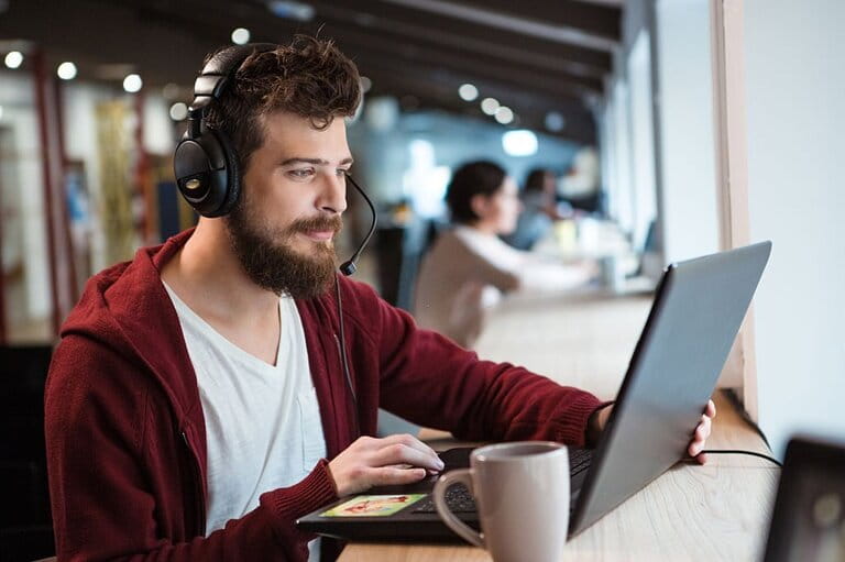 Men in dark hoodie and white t-shirt focus on using headphones and laptop