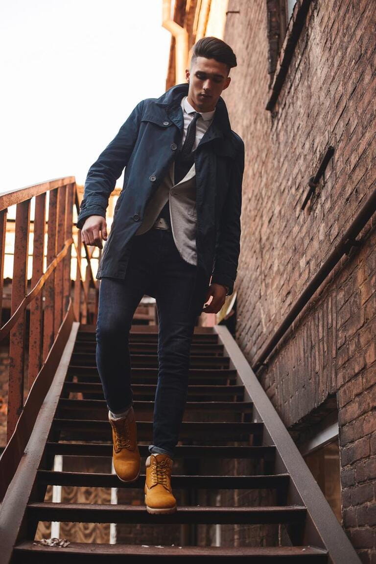 Young hipster man on stairs. A man wearing in a blue jacket , a white shirt, blue jeans and yellow boots Young hipster man on stairs. A man wearing in a blue jacket , a white shirt, blue jeans and yellow boots