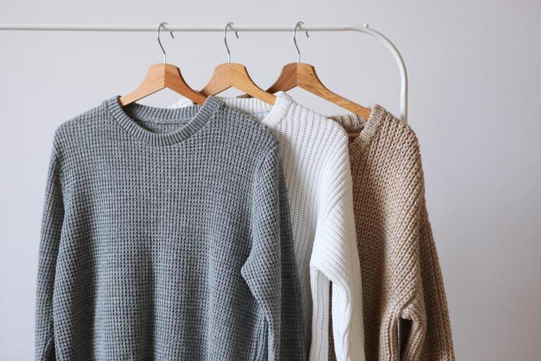 Warm sweaters on a wardrobe hanger on a light background. Autumn, winter clothes. Warm sweaters on a wardrobe hanger on a light background. Autumn, winter clothes.