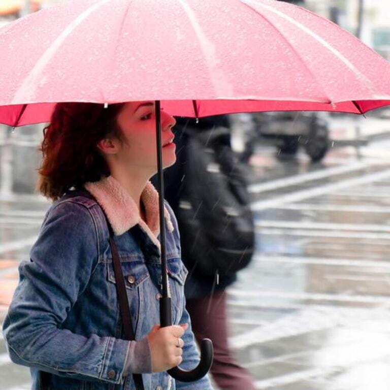 One young woman in denim jacket walking under red umbrella on a rainy day