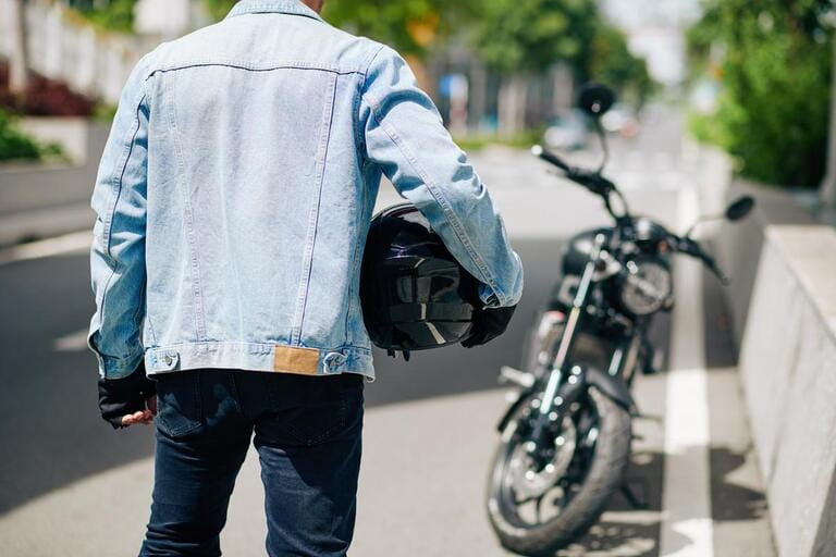 Man in denim jacket standing with motorcycle helmet, view from the back