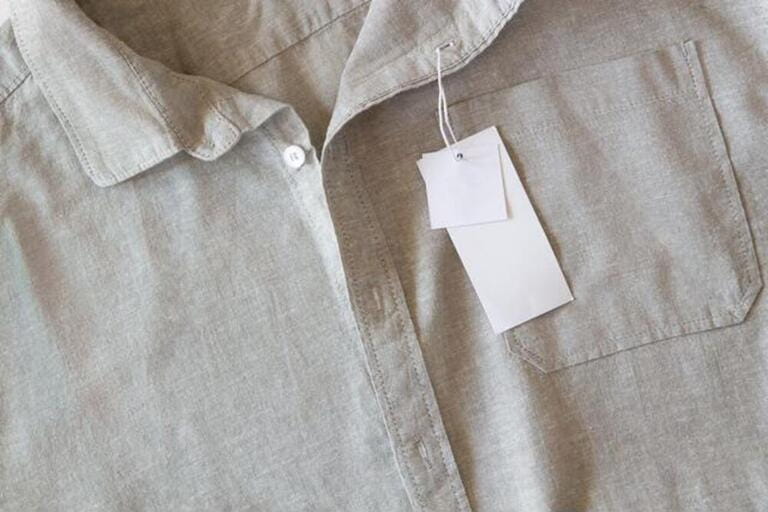 Blank price label tag paper card on natural linen shirt. Clothes label tag mockup template with copy space for brand, text, price. Top view, copy