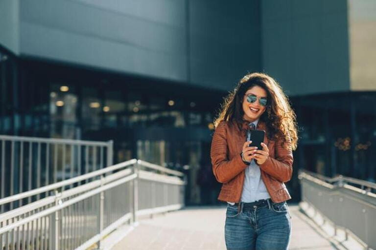 Young modern woman in brown leather jacket using smartphone in the city Young modern woman in brown leather jacket using smartphone in the city