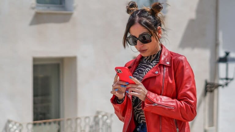 Influential young woman in ruby leather jacket viewing her likes before taking a photo Influential young woman in ruby leather jacket viewing her likes before taking a photo