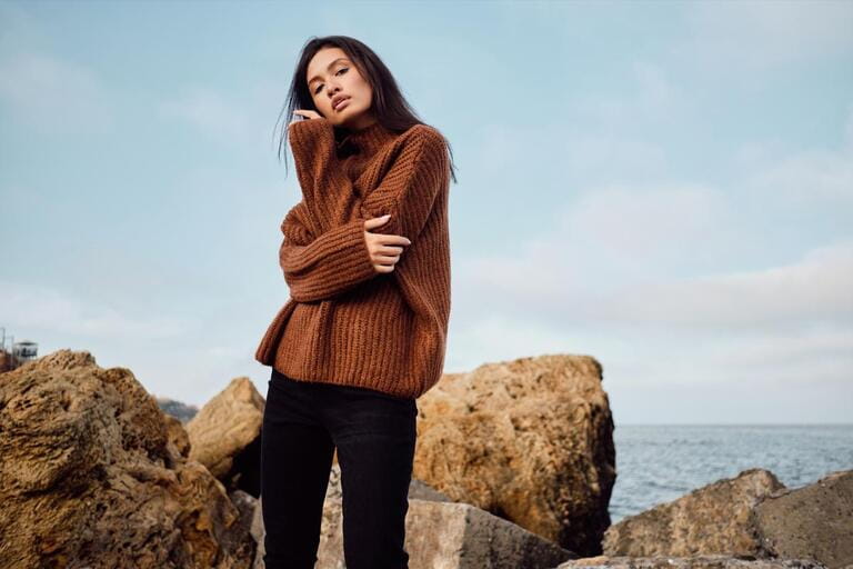 Attractive casual Asian girl in cozy knitted sweater sensually posing by the sea