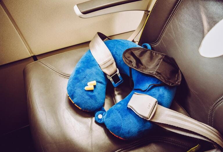 Blue soft traveling pillow, noise removing ear plugs and sleeping mask, in plane cabin on passenger seat, comfortable cozy traveling concept, composition.