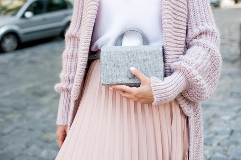 Fashionable young blond woman wearing rose cardigan, beige midi skirt and grey leather belt bag.