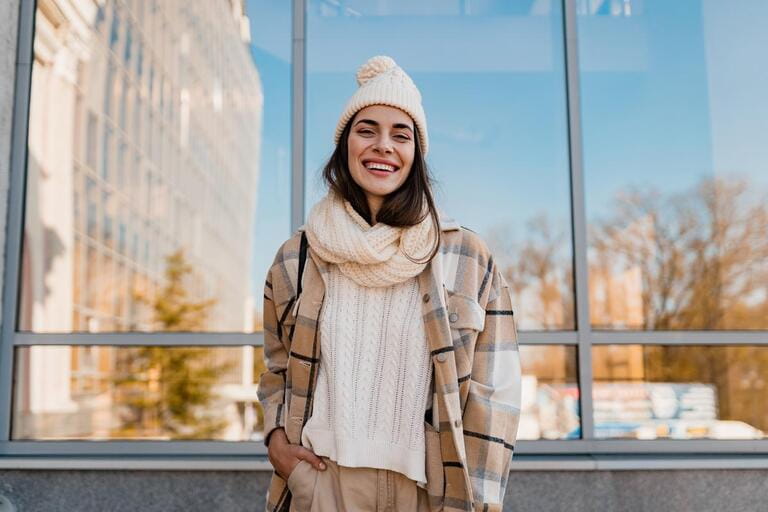 stylish attractive young smiling woman walking in street in winter outfit with coffee wearing checkered coat, white knitted hat and scarf, happy mood, fashion style trend