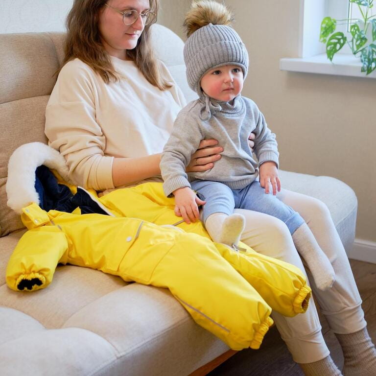 Child is dressed in warm winter clothes for a walk outside. Woman mother puts clothes on toddler baby boy for cold weather. Kid age one year five months in the home living room Child is dressed in warm winter clothes for a walk outside. Woman mother puts clothes on toddler baby boy for cold weather. Kid age one year five months in the home living room
