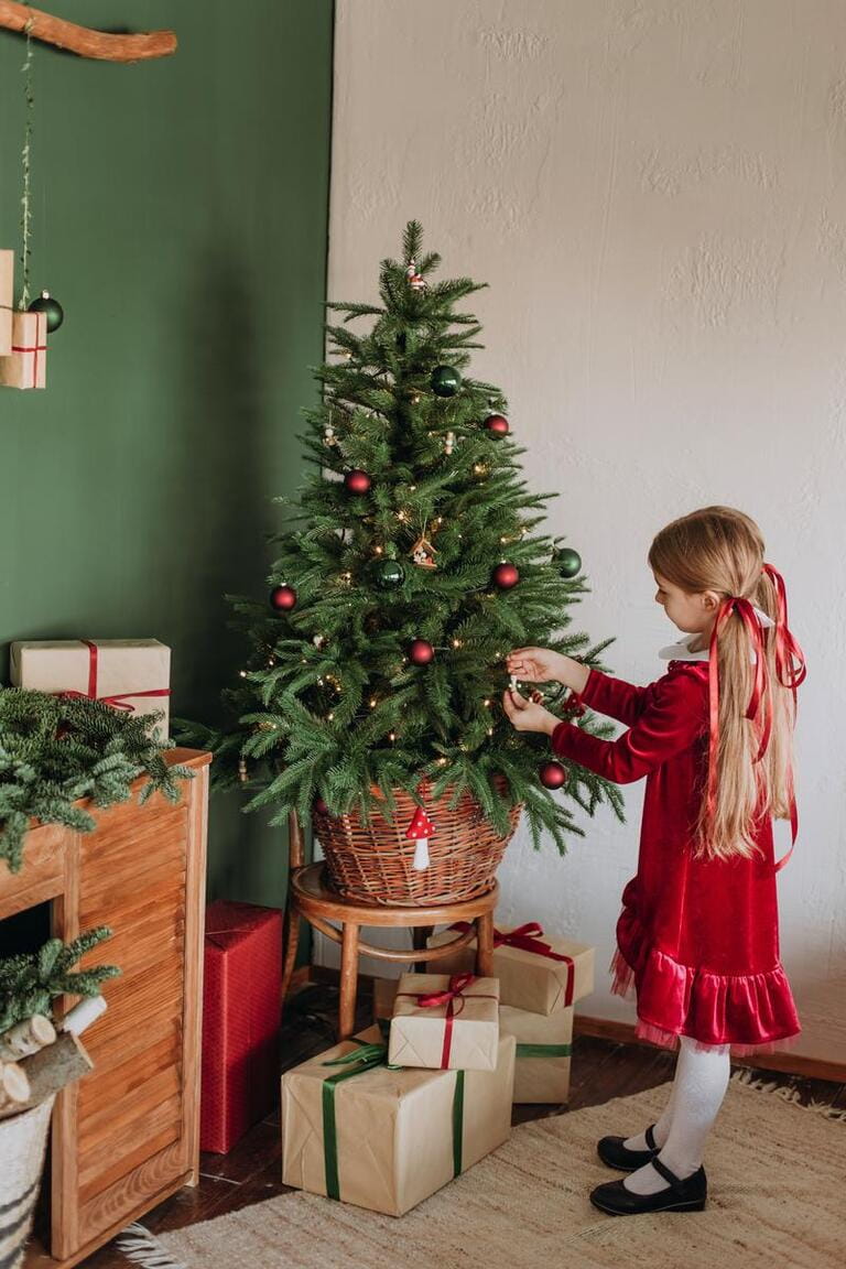 girl in a burgundy dress decorates a Christmas tree in a rustic room