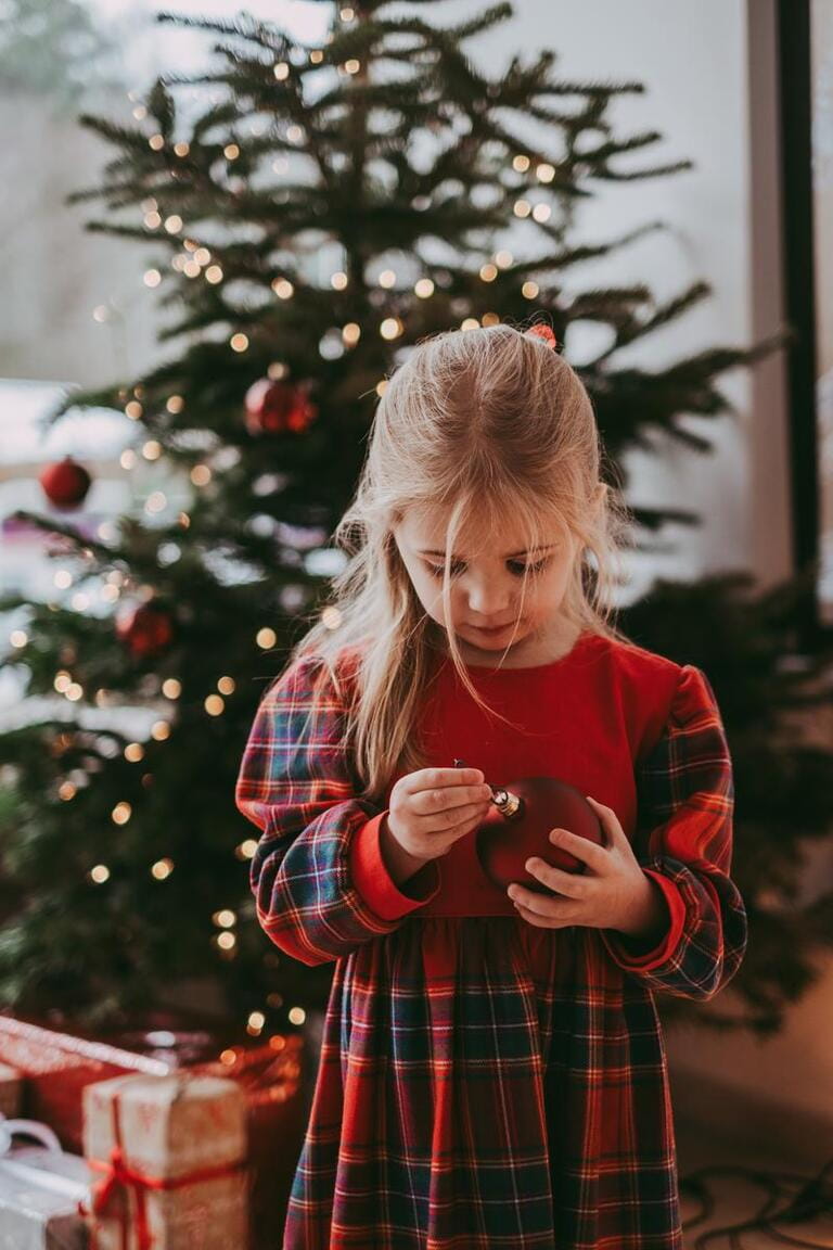 Adorable blond caucasian baby preschool girl in red dress dressing christmas tree with balls. Atmosphere of holidays, new year, waiting for Santa. Happy moment, presents Adorable blond caucasian baby preschool girl in red dress dressing christmas tree with balls. Atmosphere of holidays, new year, waiting for Santa. Happy moment, presents