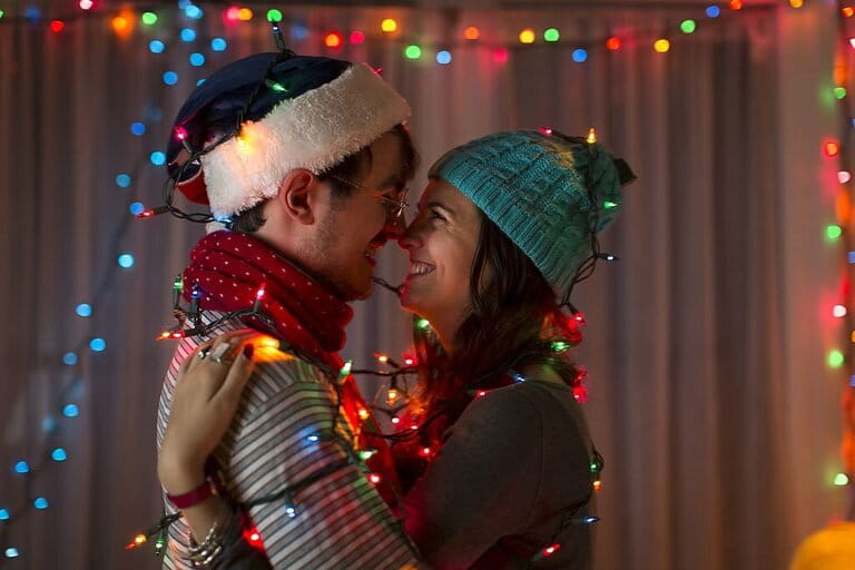 Romantic young couple wrapped in decorative lights at christmas