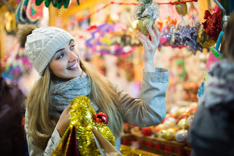 Portrait of joyful smiling blonde girl choosing gifts at Christmas market in evening time