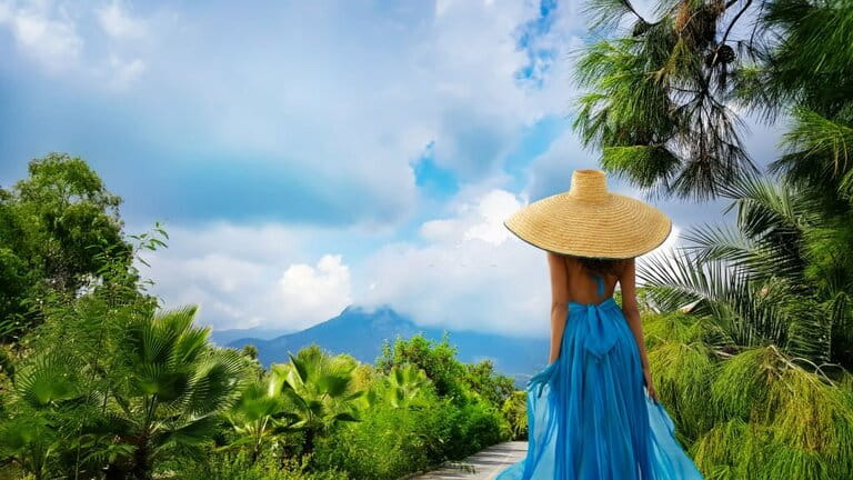 Rear view of Woman wearing Asian straw hat during summer vacation. Traveler girl wearing a blue dress looking at the mountain landscape. Tropical Jungle Resort destination