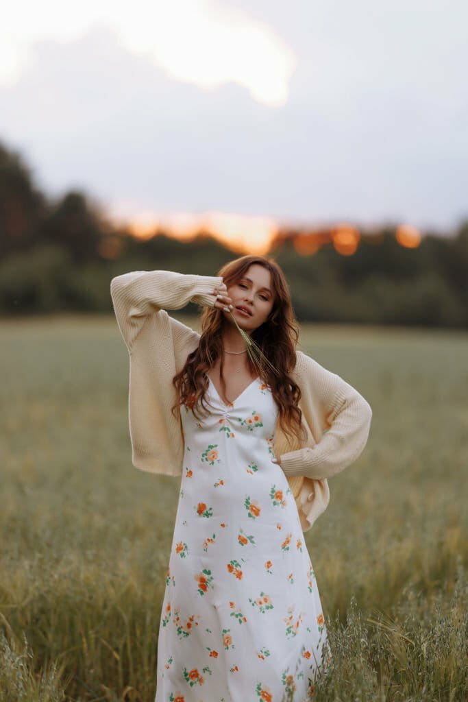 Young woman with long hair posing while standing in a wheat field with tall grass