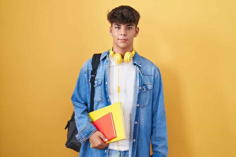 Hispanic teenager wearing student backpack and holding books with a happy and cool smile on face. lucky person. Hispanic teenager wearing student backpack and holding books with a happy and cool smile on face. lucky person.