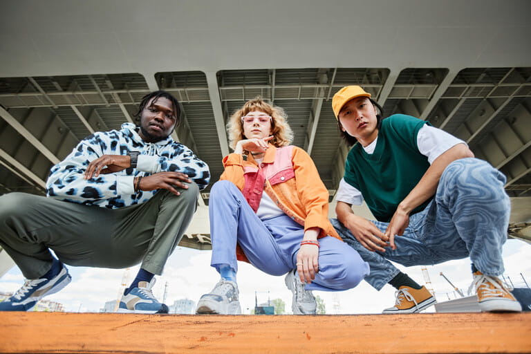 Group of three young people wearing street style clothes outdoors while sitting on stairs in urban area and looking at camera Group of three young people wearing street style clothes outdoors while sitting on stairs in urban area and looking at camera