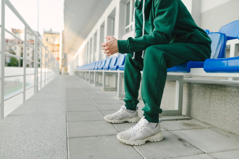 Cropped photo of a young man's legs in a green suit and bloodsuckers, sitting alone in the stands and in pain. Cropped photo of a young man's legs in a green suit and bloodsuckers, sitting alone in the stands and in pain.