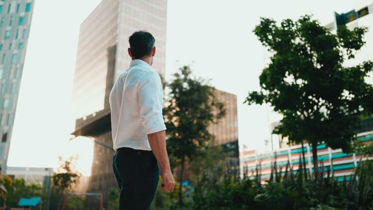 Mature businessman with neat beard wearing white shirt standing in financial district in city. Successful man looks around against the background of modern buildings Mature businessman with neat beard wearing white shirt standing in financial district in city. Successful man looks around against the background of modern buildings