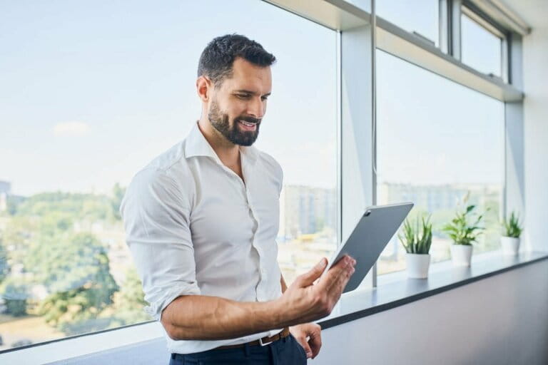 Handsome businessman using digital tablet in office leaning against window Handsome businessman using digital tablet in office leaning against window