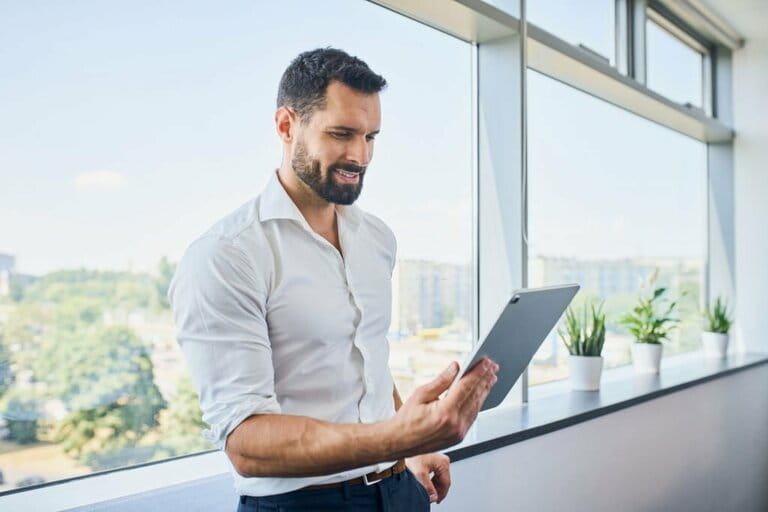 Handsome businessman using digital tablet in office leaning against window