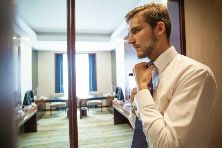 People, business, fashion and clothing concept - close up of man in shirt getting dressed and adjusting tie on neck at home.