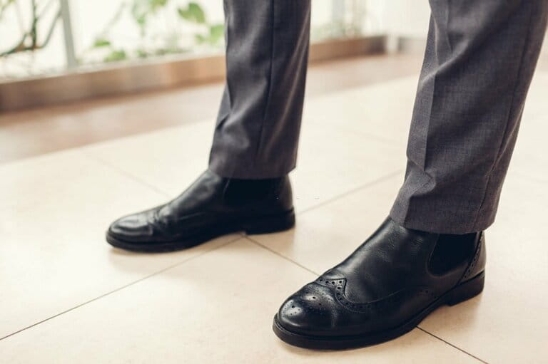 Man wearing black chelsea leather shoes and pants in shopping mall. Close-up of male feet