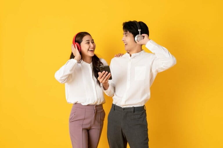 Two young handsome Asian couples using smartphone and headphones listening to music isolated on yellow background Two young handsome Asian couples using smartphone and headphones listening to music isolated on yellow background