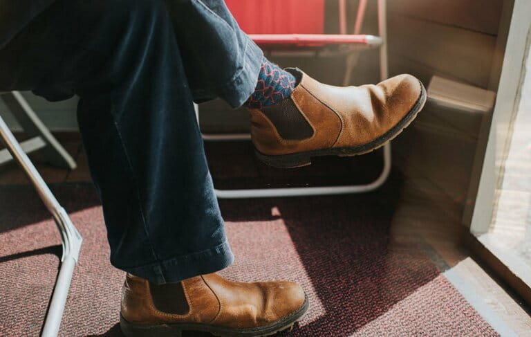 Male wearing Brown Leather Chelsea Boots, legs crossed at the knee, sitting in a sun room. Male wearing Brown Leather Chelsea Boots, legs crossed at the knee, sitting in a sun room.