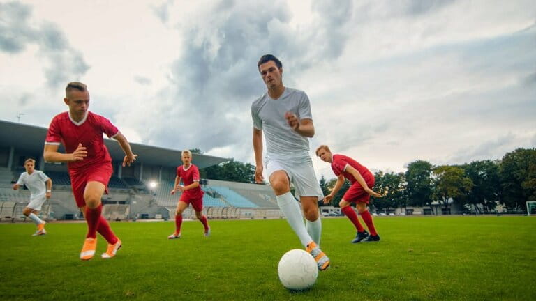 The professional football player leads with a ball, dribbles expertly and bypasses his opponents' sliding tackles. Two professional soccer teams are playing. Low angle shot The professional football player leads with a ball, dribbles expertly and bypasses his opponents' sliding tackles. Two professional soccer teams are playing. Low angle shot