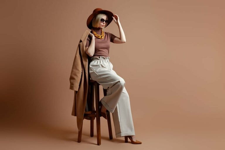 Fashionable young woman in elegant hat sitting on chair on brown background Fashionable young woman in elegant hat sitting on chair on brown background