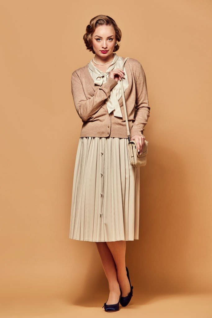 A beautiful woman wearing vintage clothes stands with a serious expression and looks at the camera against a beige background A beautiful woman wearing vintage clothes stands with a serious expression and looks at the camera against a beige background