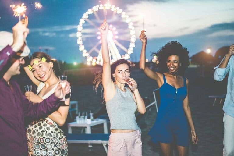 Happy friends having beach party after sunset with fireworks and drinking champagne - Happy young people dancing outdoors - Focus on the center girl's face Happy friends having beach party after sunset with fireworks and drinking champagne - Happy young people dancing outdoors - Focus on the center girl's face