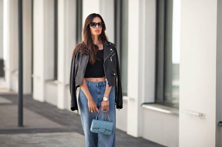 Portrait of gorgeous brown-haired woman standing on the street. Fashion model wearing black leather jacket, jeans, short shirt, small handbag on a chain. Street style Portrait of gorgeous brown-haired woman standing on the street. Fashion model wearing black leather jacket, jeans, short shirt, small handbag on a chain. Street style