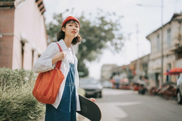 Young Asian Chinese girl waiting for transportation on the side of an old street carrying a skateboard Young Asian Chinese girl waiting for transportation on the side of an old street carrying a skateboard