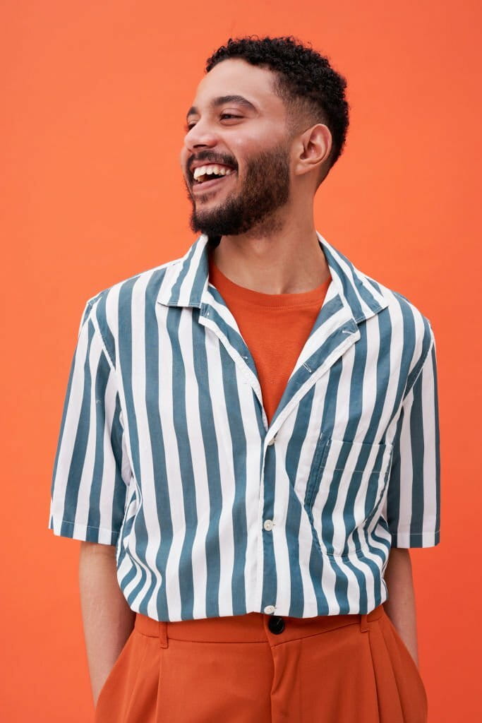 Smiling man wearing striped shirt standing against orange background